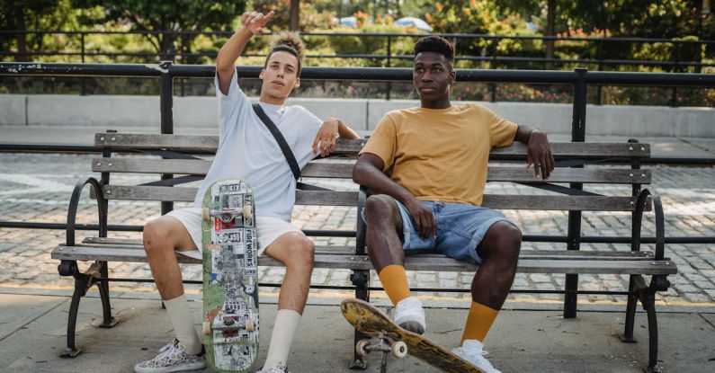 Culture Hangout - Young men sitting on bench with skateboards in park